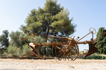 In an open field surrounded by trees, rustic antique farming tools are beautifully displayed under the midday sun