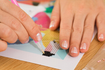 A close-up of a hand placing crystals on a canvas for a diamond painting project. Diamond Mosaic