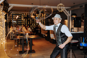 A man in a hat and vest is blowing bubbles. The bubbles are floating in the air and the man is holding a bubble wand. The scene is lively and fun
