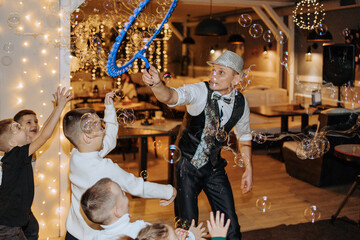 A man in a suit is blowing bubbles for a group of children. The children are standing around him, watching as he blows bubbles. The scene is lively and fun, with the children enjoying the activity