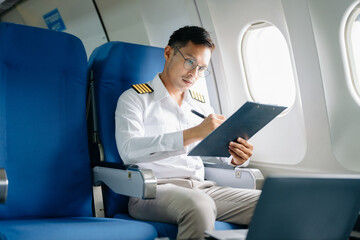 Fototapeta premium Asian Confident male pilot in uniform leaning at the passenger seat while standing inside of the airplane flight cockpit during takeoff