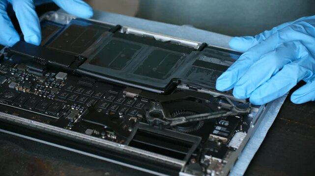 Technician in gloves carefully installs new battery block in laptop. Man ensures connection secure and properly aligned with professional approach