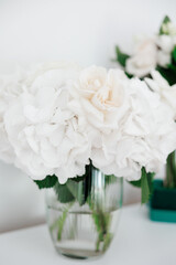 A vase of white flowers sits on a table. The flowers are white and arranged in a way that makes them look like they are blooming. The vase is clear and allows the flowers to be seen through it