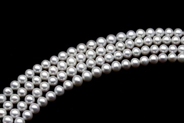 Chinese round freshwater white pearls on strands ready to become a necklace, some of the favorite materials for jewelry on black background. An organic gem that brides love for weddings.