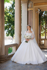 A woman in a white wedding dress is standing in front of a building with a bouquet of flowers in...