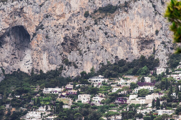 Hillside houses nestled among lush greenery at the base of rugged cliffs, showcasing a scenic and dramatic landscape in Capri Island, Italy.