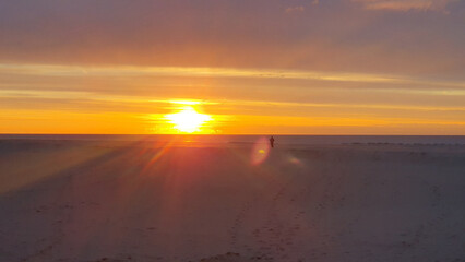 One person alone walking on a beach at sunrise.