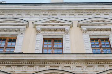 Three windows on the facade of a house with beige plaster in the central historical part of the city. Beautiful decorative architecture with reliefs, cornice and white columns in Lviv, Ukraine.