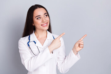 Portrait of qualified doctor woman indicate fingers empty space white coat isolated on grey color...