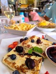 Restaurant table set with grilled cheese,garnished with strawberries,blueberries and jam. Chips and fried fish.Friends,at the restaurant eating,grilled cheese garnished with berries,jam,fish and chip 