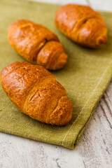 Freshly baked croissants on a green cloth, placed on a rustic white wooden table.