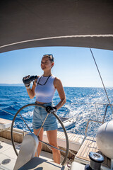 Young female captain on the yacht looking through binoculars during sailing boat control. Travel and active life. Yachting