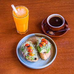 Plate with two avocado toasts, glass of fresh orange juice and cup of black coffee on wooden table
