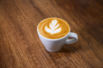 White cup of cappuccino standing on wooden table with latte art