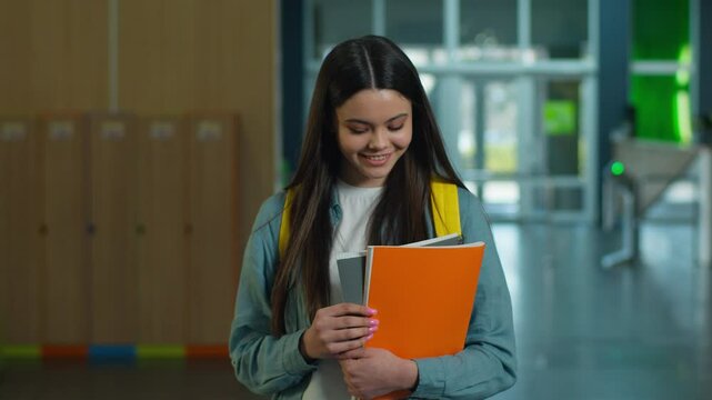 Happy smiling Caucasian student girl female schoolgirl woman pupil teenager teen walking going in school corridor walk in university hall education study hold copybooks learning go to class lesson