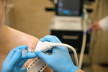 Surgeon performing ultrasound-guided shoulder arthrocentesis on female person