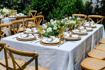 Elegant table setting being prepared for a garden party with white flowers and rattan details