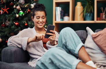 Obraz premium Happy woman, relax and typing with phone on sofa for christmas, online browsing or special deal at home. Young female person with smile on mobile smartphone for research on december offer at house