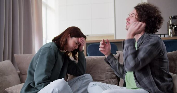 An impulsive brunette guy with curly hair in a gray T-shirt actively talks and expresses his dissatisfaction in the relationship of a brunette girl in a green jacket during an argument while sitting