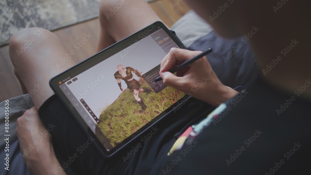 Poster boy with digital stylus and tablet in hands sits in cozy room and draws 3d model. teenager creates n