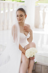 A woman in a white wedding dress sits on a ledge with a bouquet of white roses in her lap