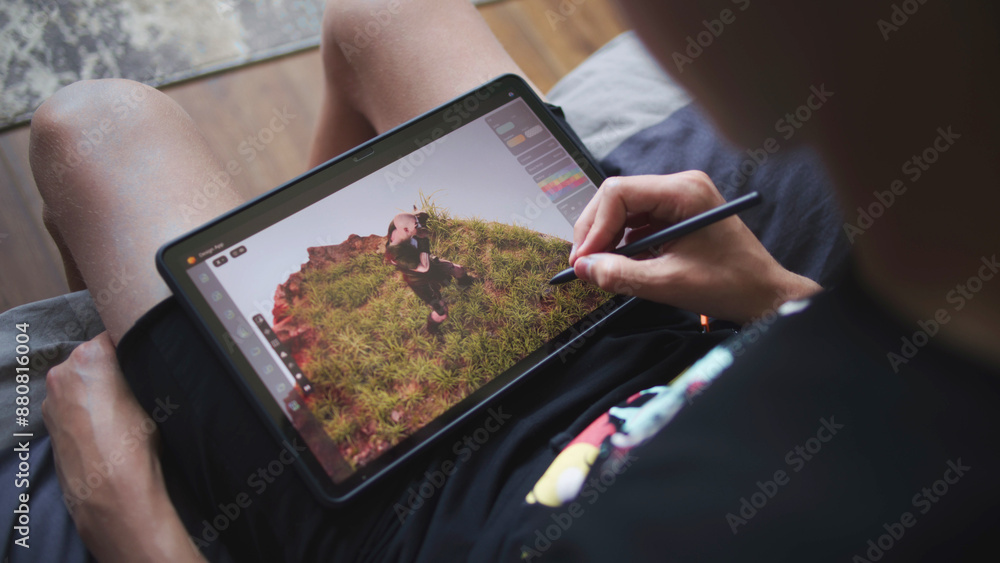 Poster boy with digital stylus and tablet in hands sits in cozy room and draws 3d model. teenager creates n