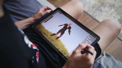 Boy with digital stylus and tablet in hands sits in cozy room and draws 3d model. Teenager creates new skin using 3d modeling program. Young game designer remote studying. Game development. Close up.