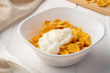 Cornflakes with yoghurt in white bowl on wood table