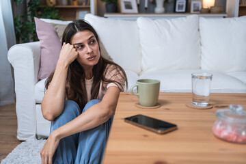 Young depressed sad anxious and worried woman sitting alone on the floor waiting for phone call from hospital. Sick stressed woman expecting medical results from doctor. Health care and medicine