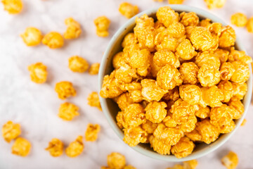 Sweet caramel popcorn in a bowl on a wooden background. Salted caramel popcorn. Caramel sauce. Close up. Topping. Place for text. Copy space