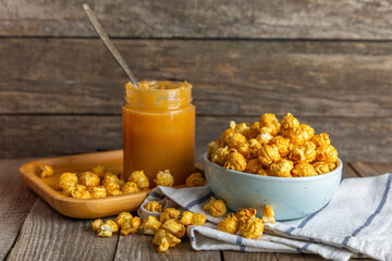 Sweet caramel popcorn in a bowl on a wooden background. Salted caramel popcorn. Caramel sauce. Close up. Topping. Place for text. Copy space