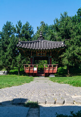 Old red wooden gazebo. The path is paved with stones to an old Korean-style wooden gazebo