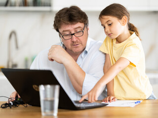 Father helps daughter do homework using laptop