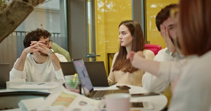 Group of company employees actively discussing ideas during a meeting in a modern office environment. They are collaborating on a project with laptops and documents.