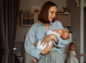 Close-up portrait of tender young mother holding newborn baby in her arms, wearing blue shirt at...