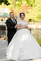 A bride and groom are posing for a picture in front of a fence. The bride is wearing a white dress and the groom is wearing a black suit. Scene is happy and celebratory