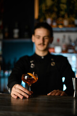 Cocktail glass with elite alcohol in hand of blurred man in black clothes