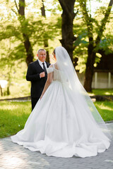 A bride and groom stand in a park, with the bride wearing a white dress and the groom wearing a black suit