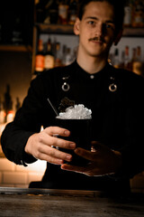 Handsome guy with mustache and black shirt stands with a black glass with ice