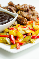 A plate of meat and vegetables with a sauce on the side