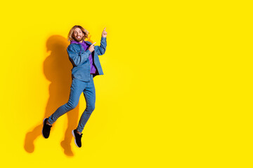 Full size photo of nice young man jump indicate fingers empty space wear denim jacket isolated on yellow color background