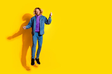 Full size photo of nice young man jump empty space wear denim jacket isolated on yellow color...