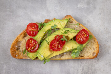 A slice of toasted sour dough bread with avocado and tomato on top