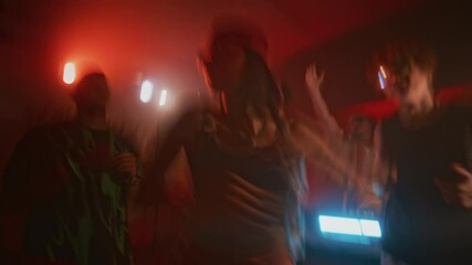 Blurred handheld shot of fashionable lady in y2k outfit actively dancing during retro rave party in nightclub with red neon light and repeated flashes