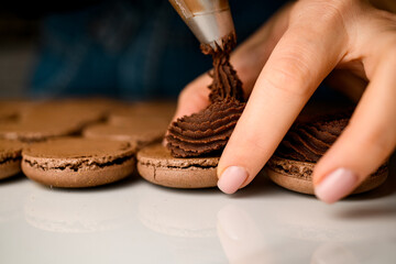 Hands of chef fills a macarons preparations with help of bag with whipped cream