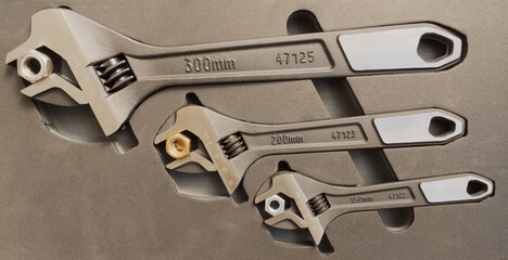 Closeup of three different sized adjustable wrenches in a fitted case, each holding a steel nut in the open jaws.