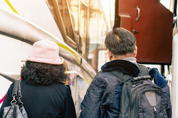 Back view of senior happy tourist couple at bus station. Happy lovers traveler relaxing and enjoying with traveling by bus on holiday. Woman with hat getting in a bus at the station. Happy journey.