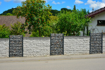 Moderner Sichtschutzzaun aus mit Naturstein gefüllten Gabionen und Betonstein-Mauer um ein neu bebautes Grundstück © Hermann