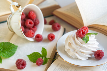 Sweet raspberries in a porcelain cup on a table with books.
