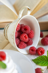 Sweet raspberries in a porcelain cup on a table with books.